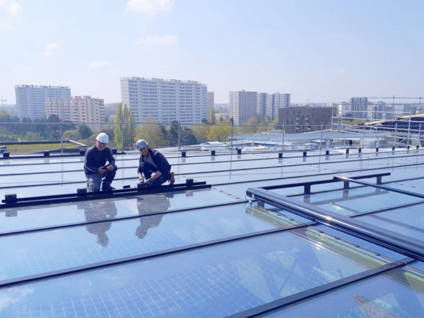 Des équipiers d'Énergère en train d'installer un store extérieur enrouleur sur la verrière d'un bâtiment.
Pour leur sécurité, ils portent un casque, et un filet est tendu sous la verrière.
