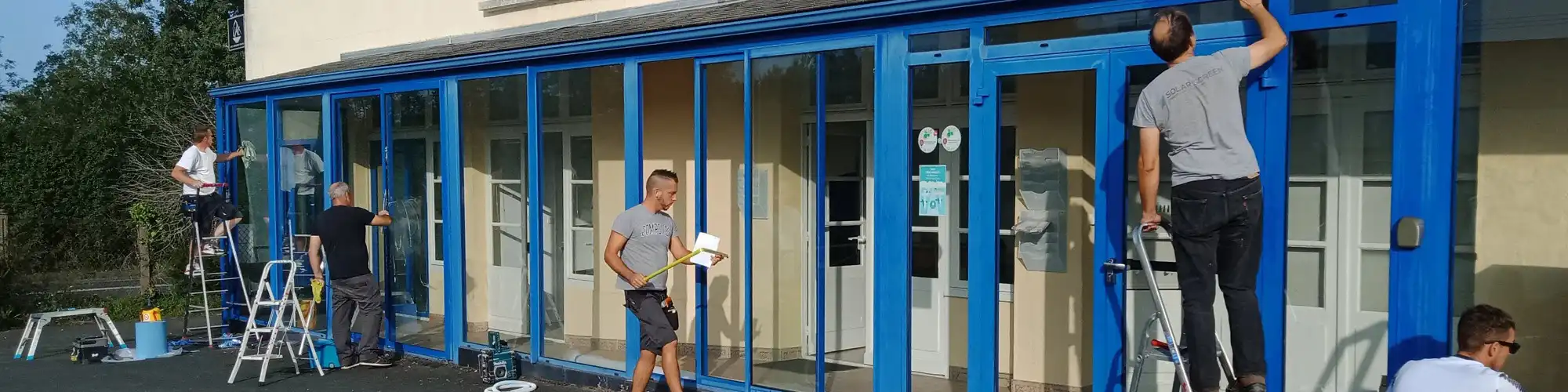 Équipes d'Énergère en train de poser du film adhésif de protection solaire sur la véranda des bureaux d'Énergère.